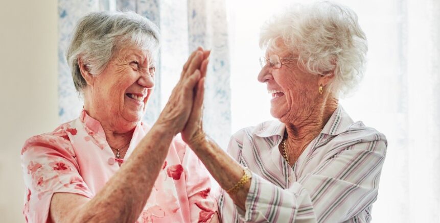 Assisted Living Lifestyle Option Box. Image is of Two senior ladies high fiving and smiling